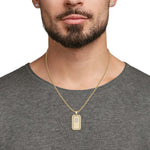 Man wearing a gold necklace with a rectangular pendant on a plain background